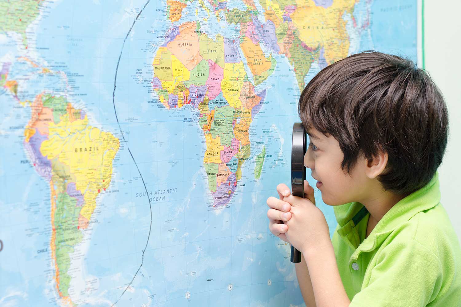 Un enfant regarde une mappemonde avec une loupe